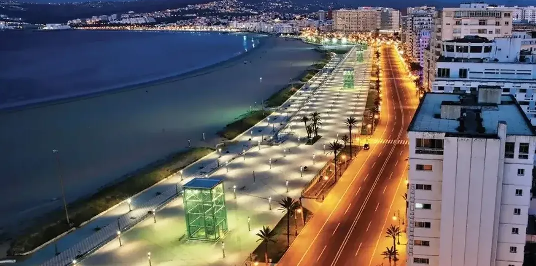 Tanger, entre histoire, nature et évolution : découvrez les lieux à ne pas manquer Tanger Vue panoramique de la corniche de Tanger la nuit, montrant les immeubles illuminés, la route bordée de lumières et la plage au loin.